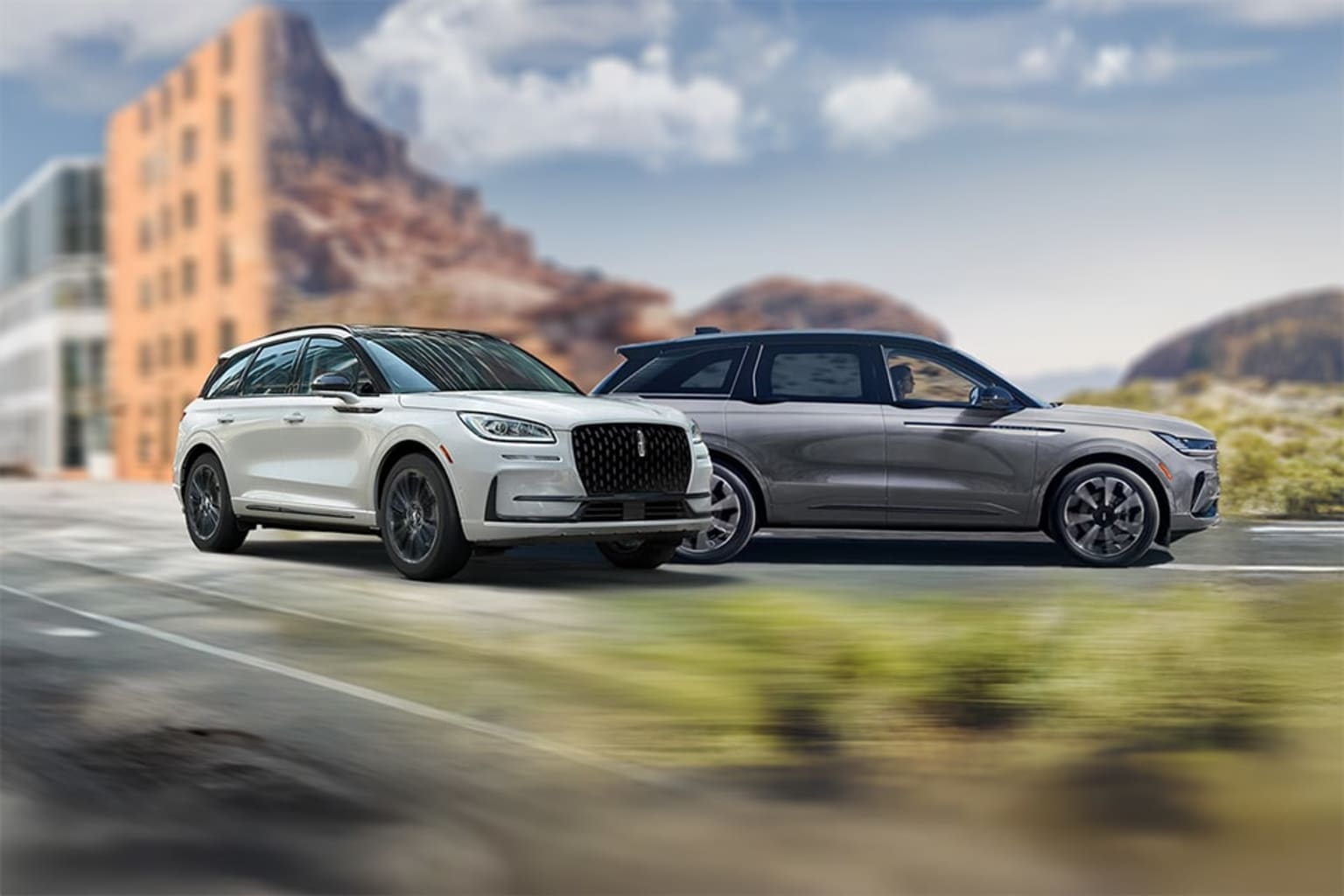 Two luxury SUVs on a wet road with a modern city skyline in the background.