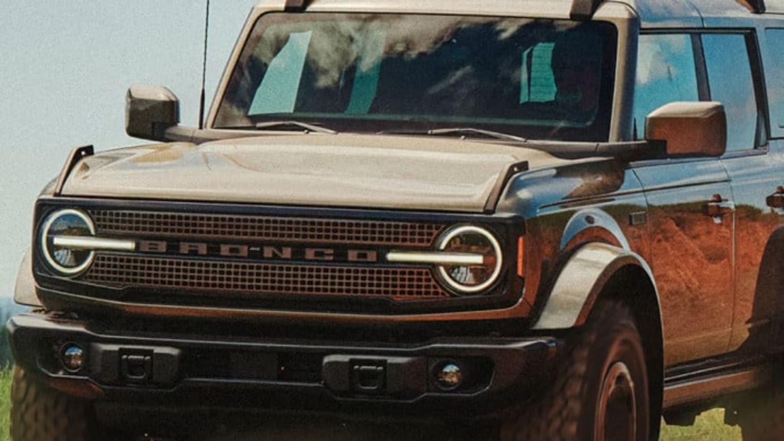 An SUV with a tan color and a black grille is parked in a dry, grassy field with a dirt road in the background.