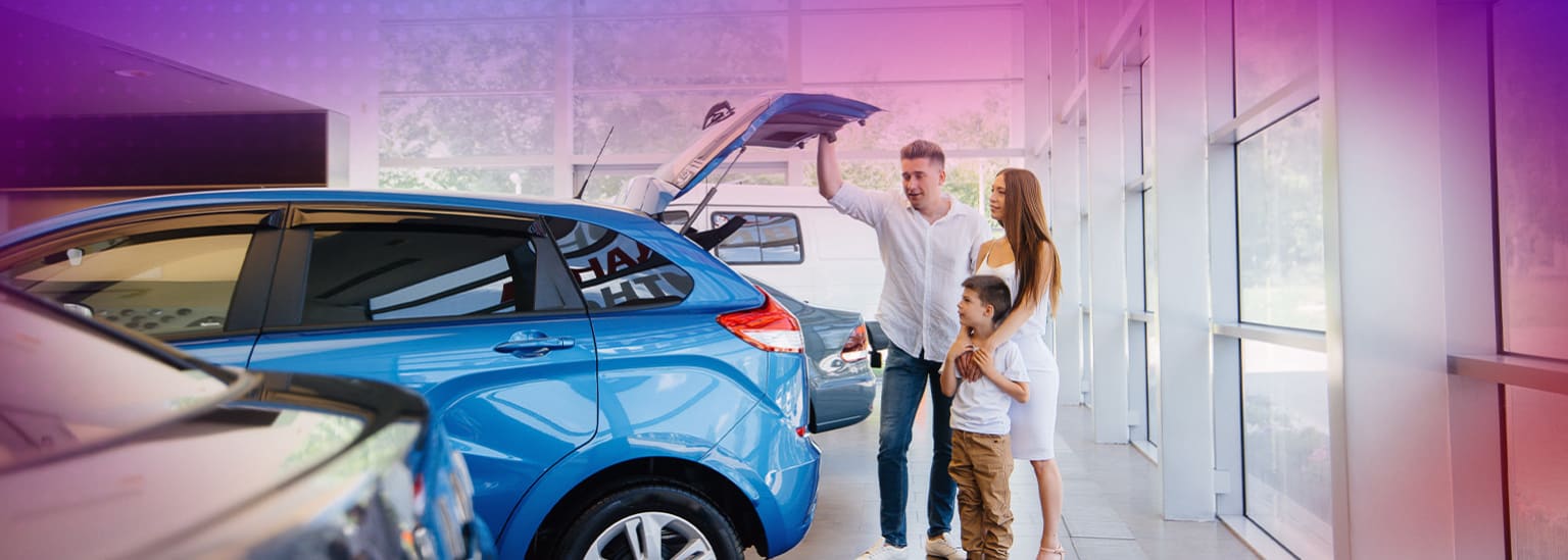 A young couple standing next to a blue car in a garage, with the car's trunk open and a person's hand visible inside.