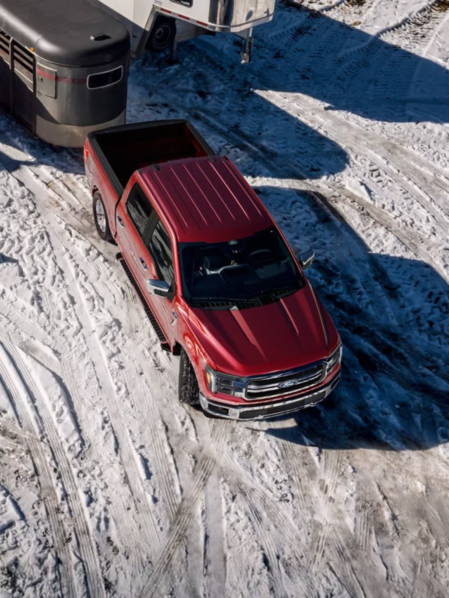A red pickup truck parked on a snowy surface with a large trailer in the background.