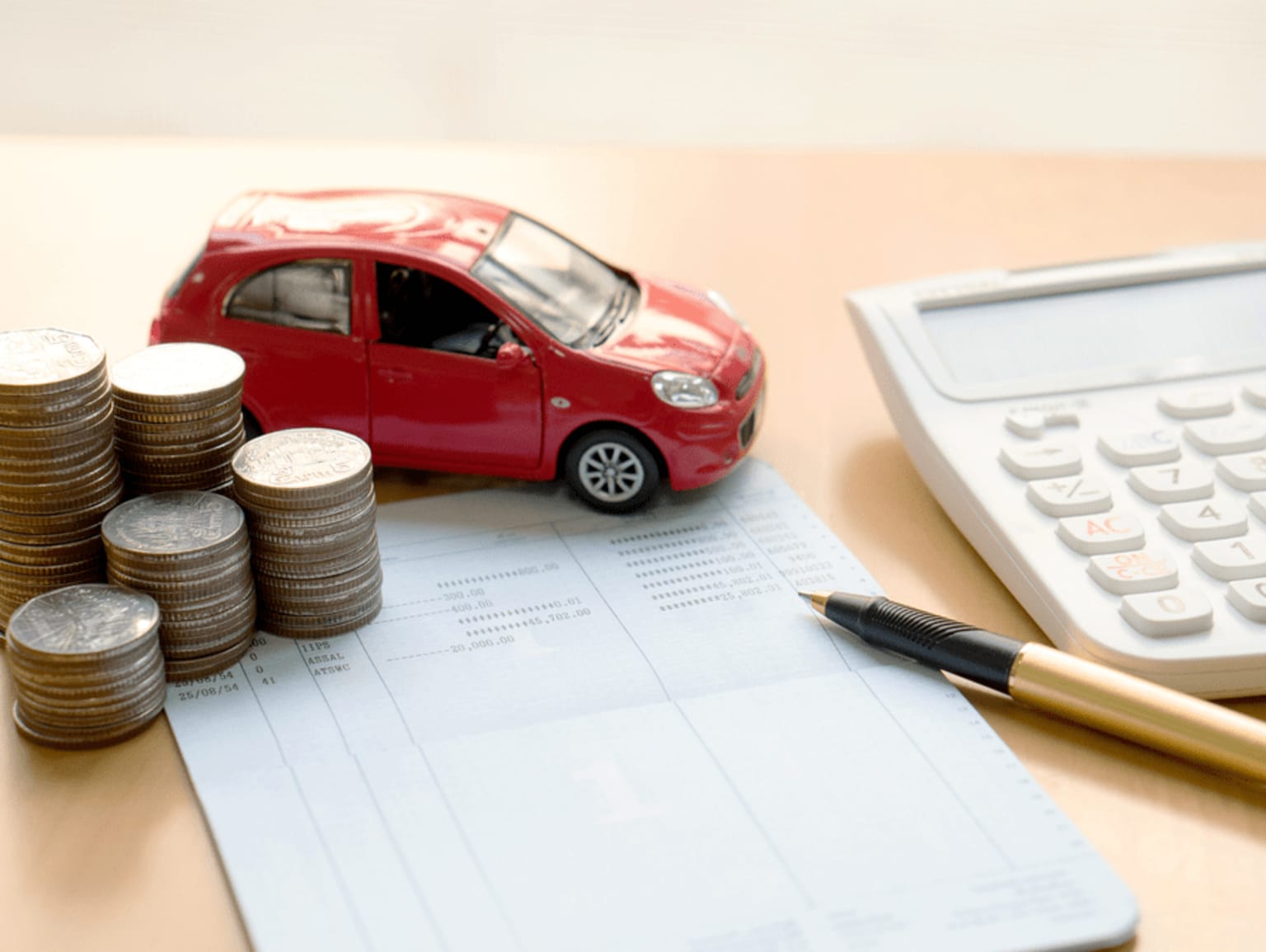 Financial planning or budgeting image for vehicle purchase with a red toy car, stacks of coins, a calculator, and a pen on a document or form.
