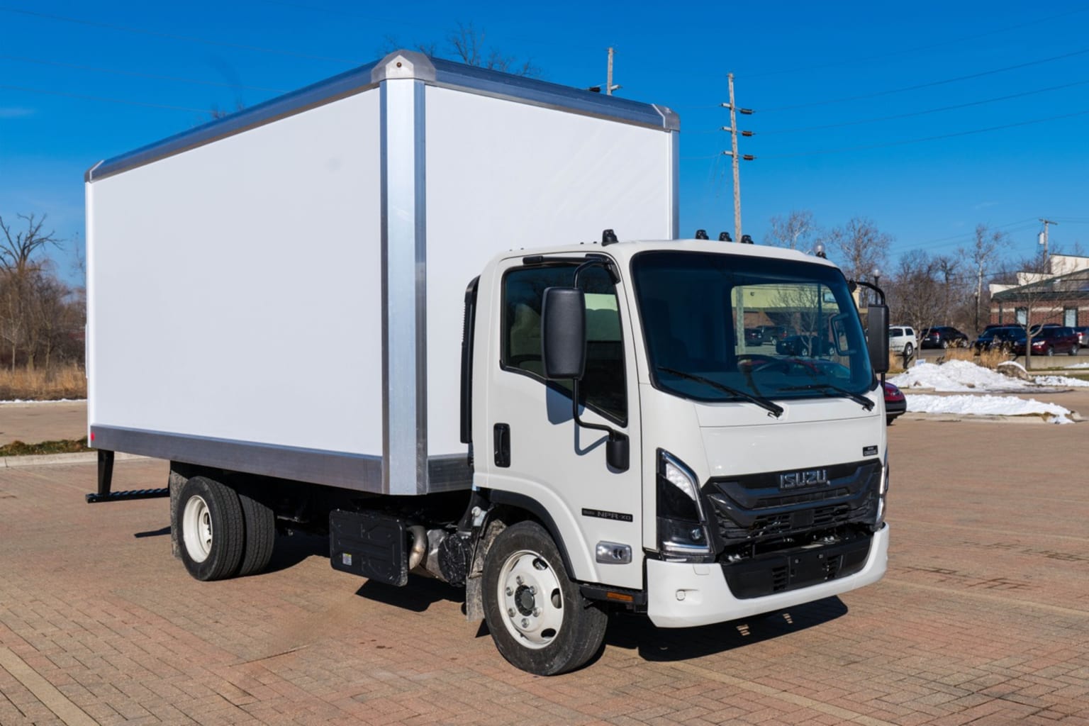 A white box truck is parked on a brick-patterned surface with a clear blue sky and buildings in the background.