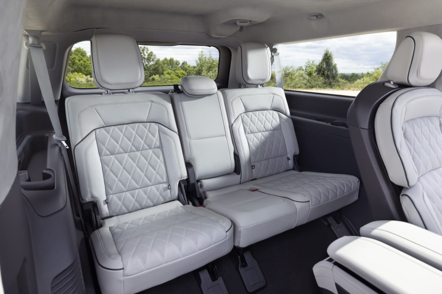 Interior of a vehicle with spacious and well-designed seating arrangement featuring comfortable white leather seats, set against a backdrop of trees and greenery.