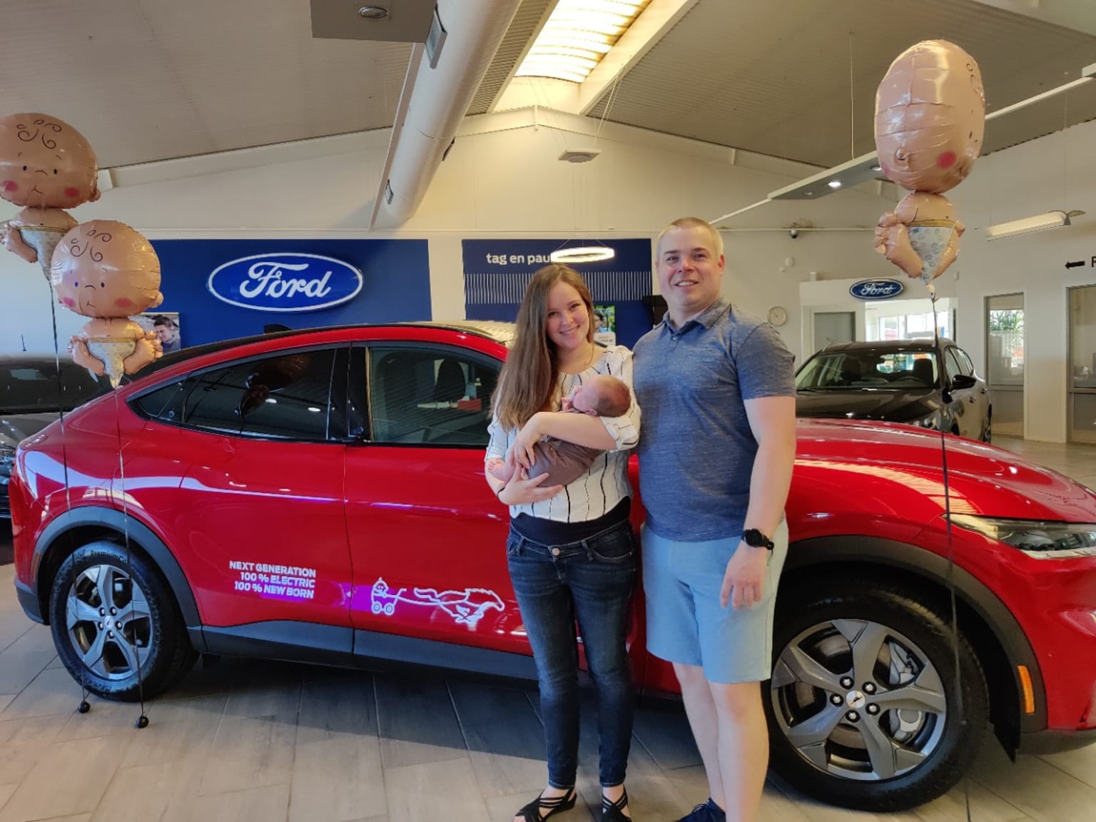 a man and a woman standing next to a red car in a dealership with balloons in the background