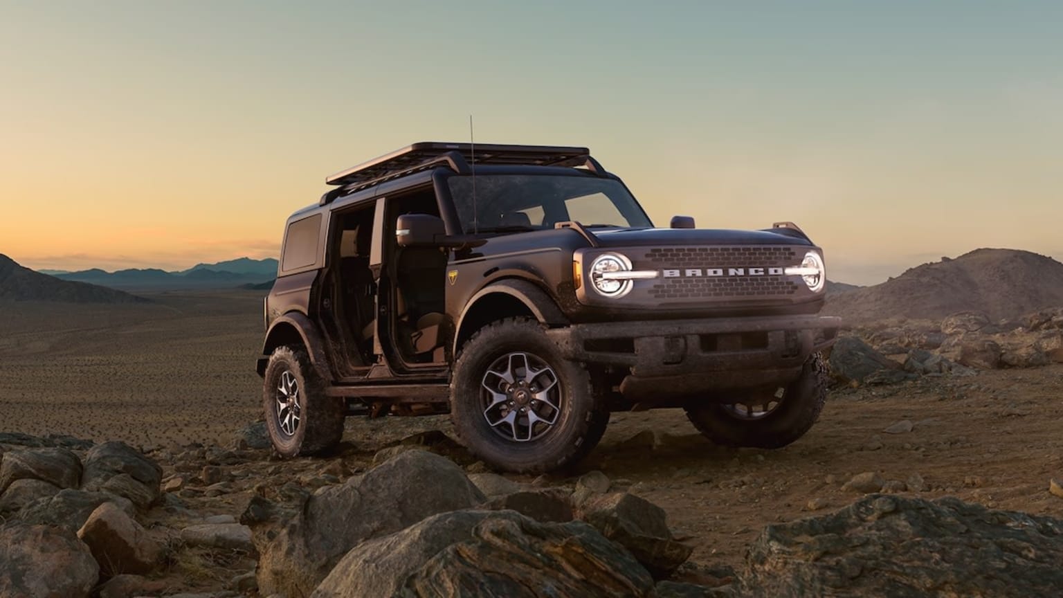 A rugged off-road vehicle navigating through a rocky, mountainous landscape at sunset, with the sky transitioning from warm hues to a clear blue.