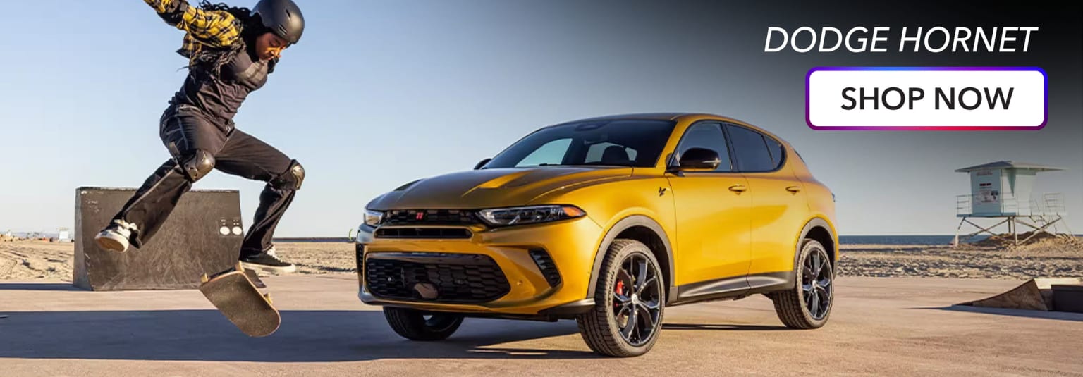 a man riding a skateboard next to a yellow sports utility vehicle on a desert road in front of a blue sky