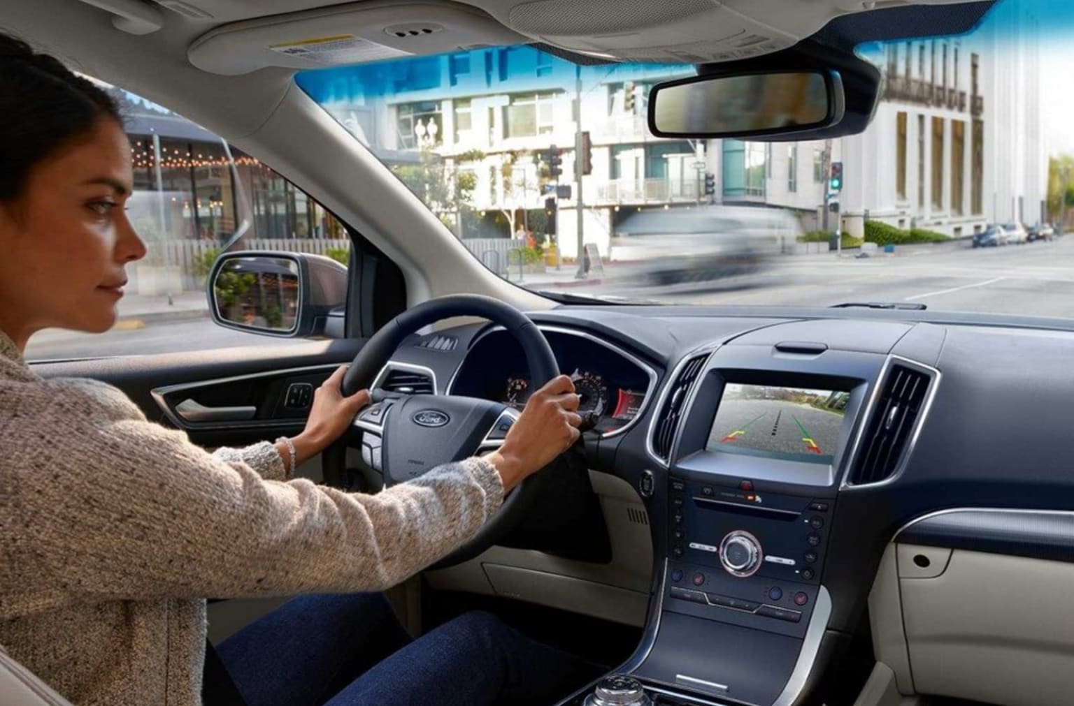 a woman driving a car on a city street with a view of the street from the driver's seat