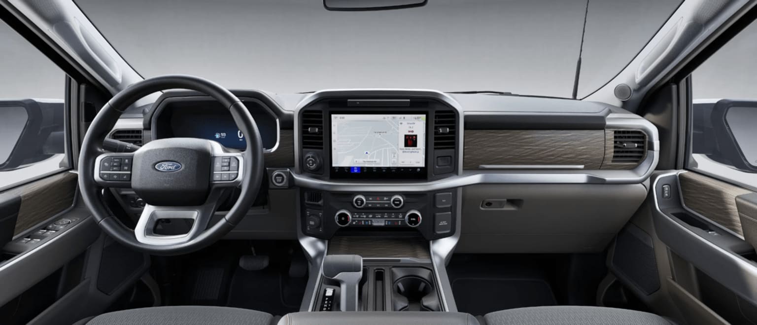 The image displays the interior of a contemporary vehicle, including a steering wheel, dashboard, and different controls and displays. The background features the front windshield and dashboard of the vehicle.
