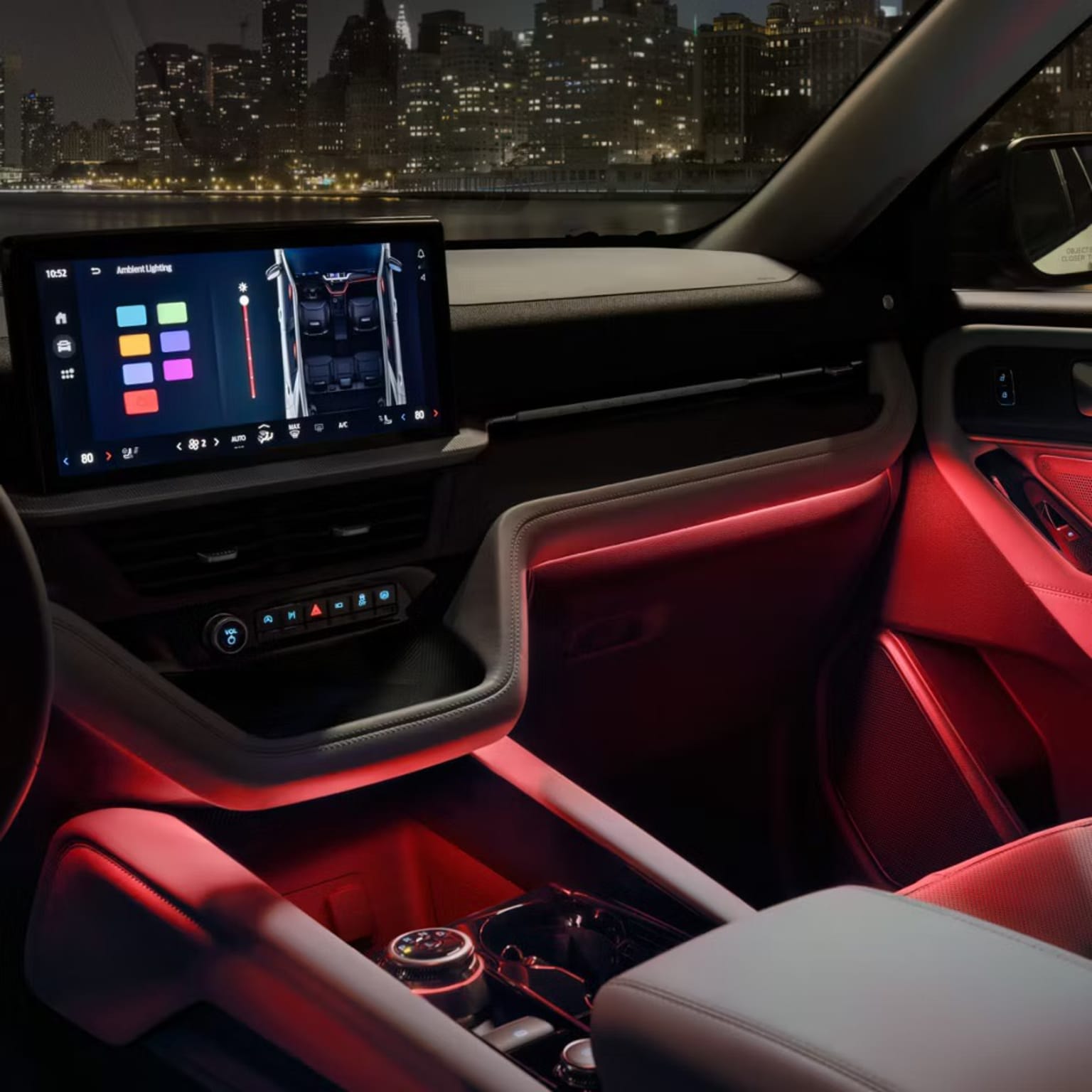Interior of a modern vehicle with a large touchscreen display, red leather seats, and a cityscape visible through the windshield in the background.