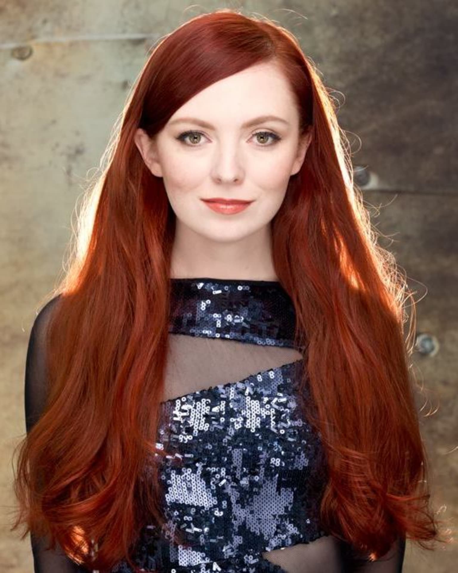a woman with long red hair wearing a black and silver dress and posing for a picture in front of a wall