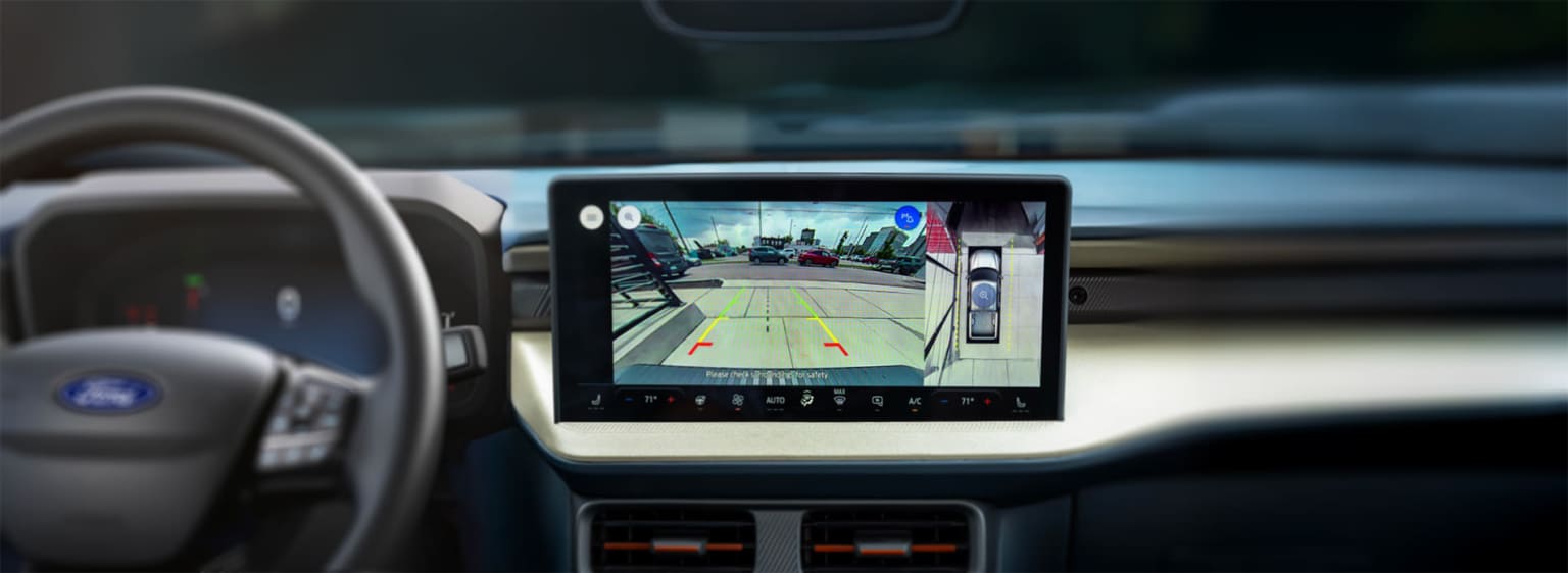 The image displays a car's dashboard with a touchscreen display showing a rear-view camera view, providing a clear visual of the surroundings behind the vehicle.