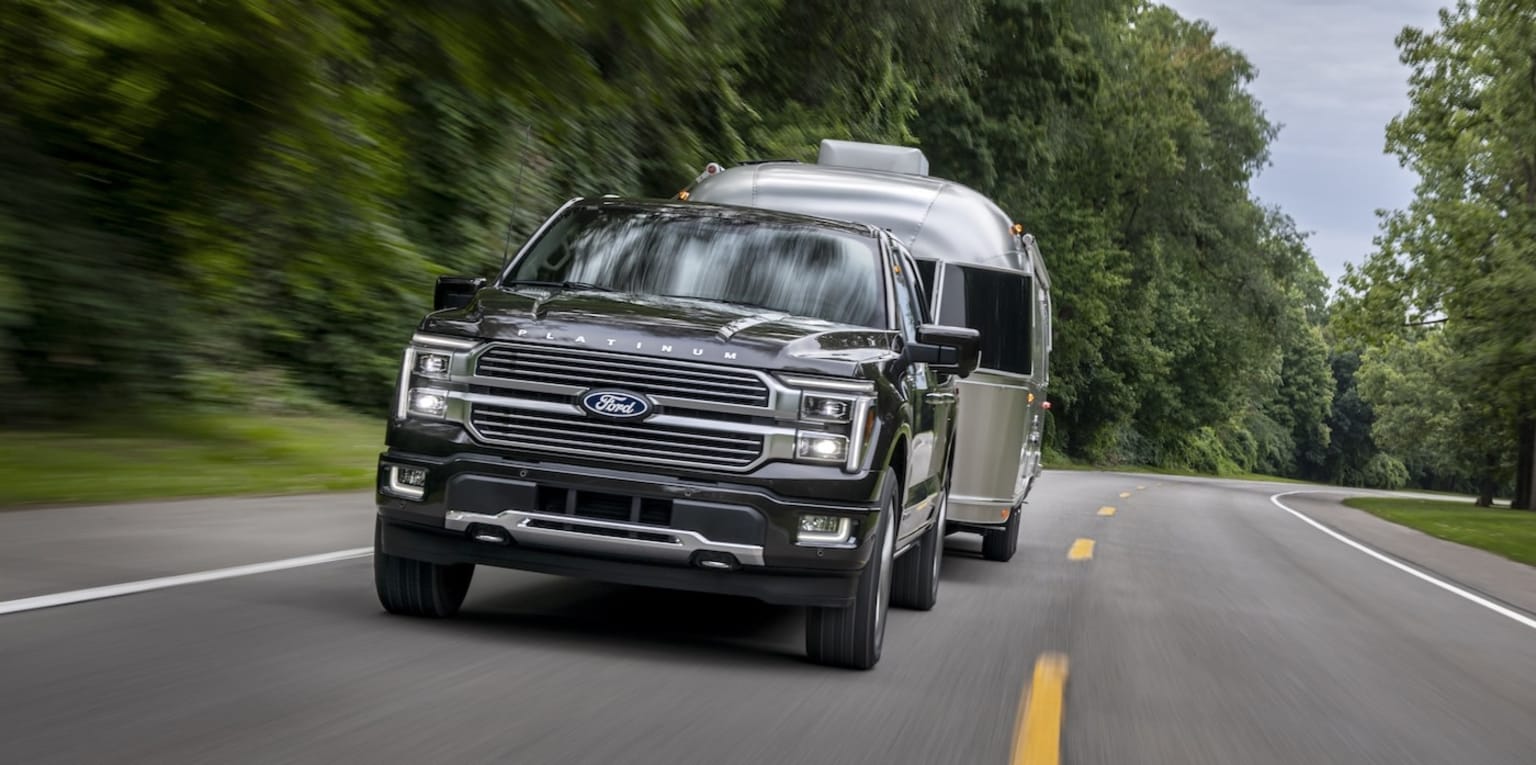 An image of a large, rugged-looking black SUV speeding down a winding road surrounded by lush, green trees and foliage.