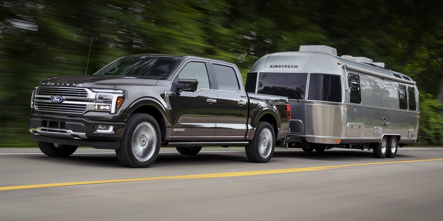 Image of a pickup truck towing a silver Airstream trailer on a scenic road surrounded by lush green foliage.
