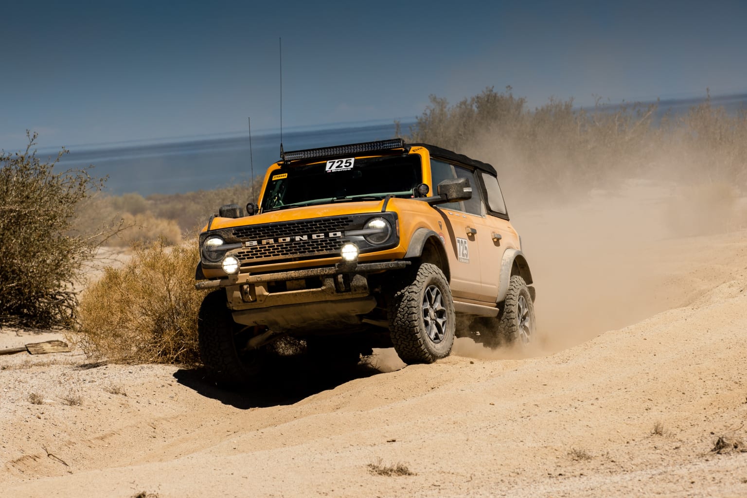 a yellow truck driving through the desert on a sunny day with a blue sky in the backgroud