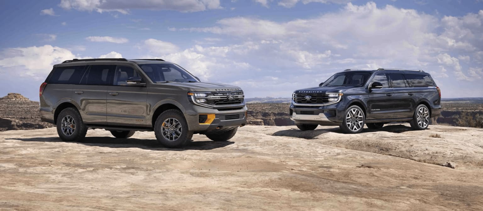 Two off-road vehicles parked on a dusty, rocky terrain with a cloudy sky in the background.
