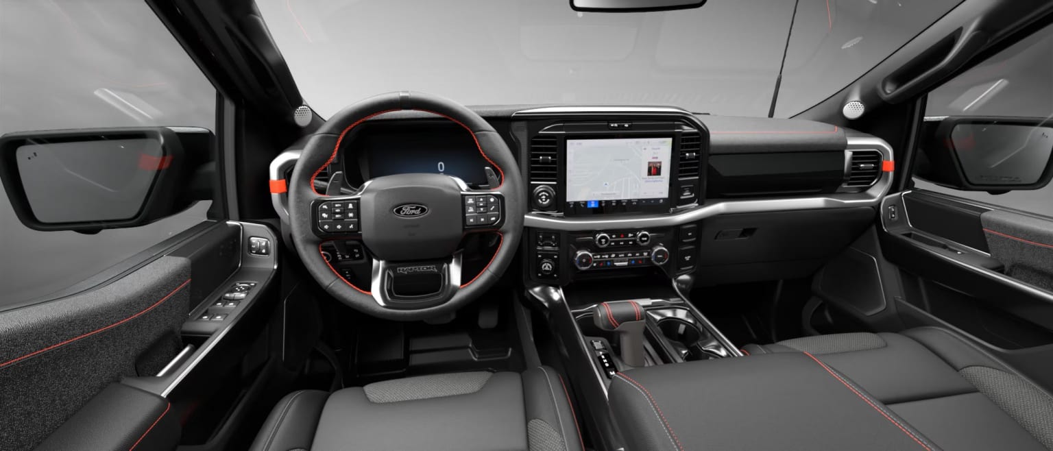 The image shows the interior of a modern vehicle with a steering wheel, dashboard, and various controls and displays visible.