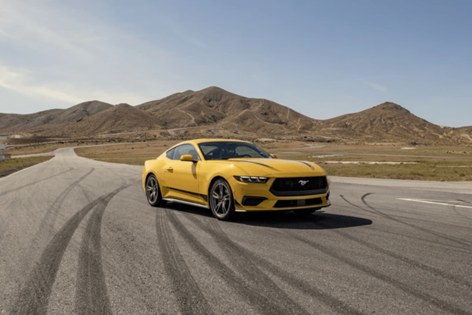 A yellow sports car is driving on a road surrounded by rugged, mountainous terrain in the background.