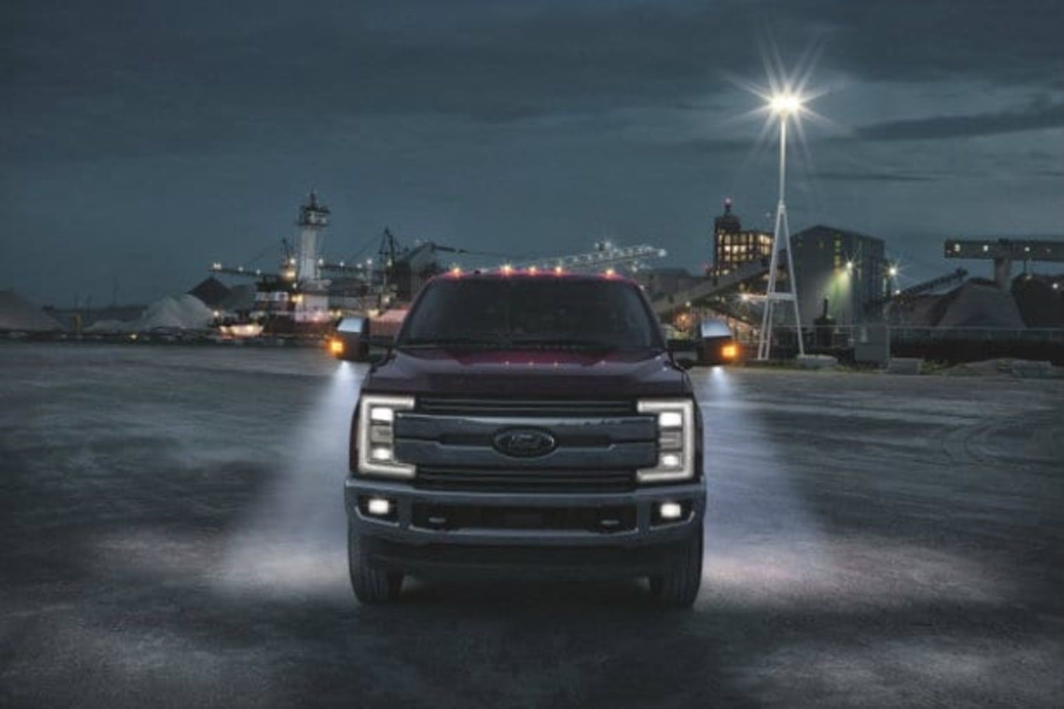 a truck parked in a parking lot at night with a city skyline in the background and lights shining on the truck