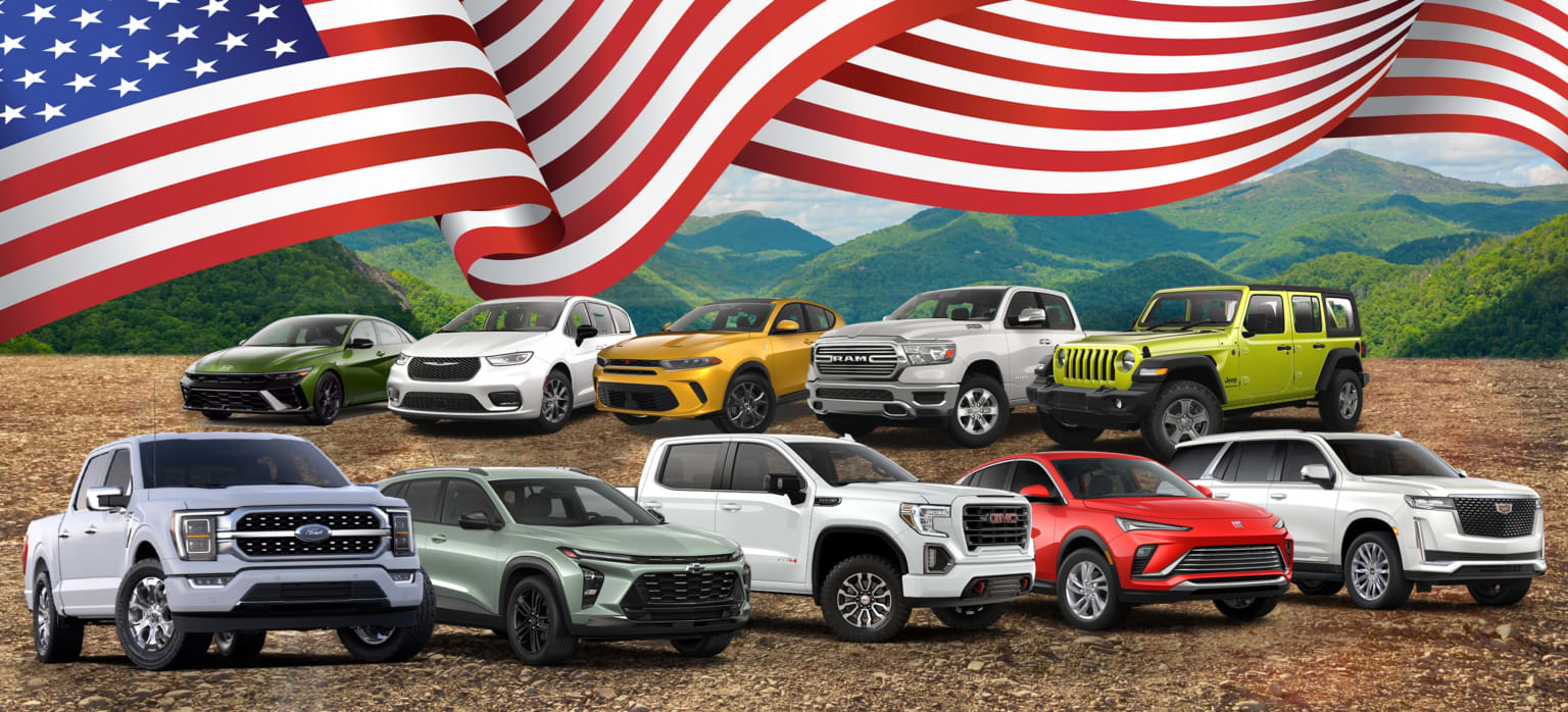 American-made vehicles on a dirt lot with green hills and an American flag in the background.