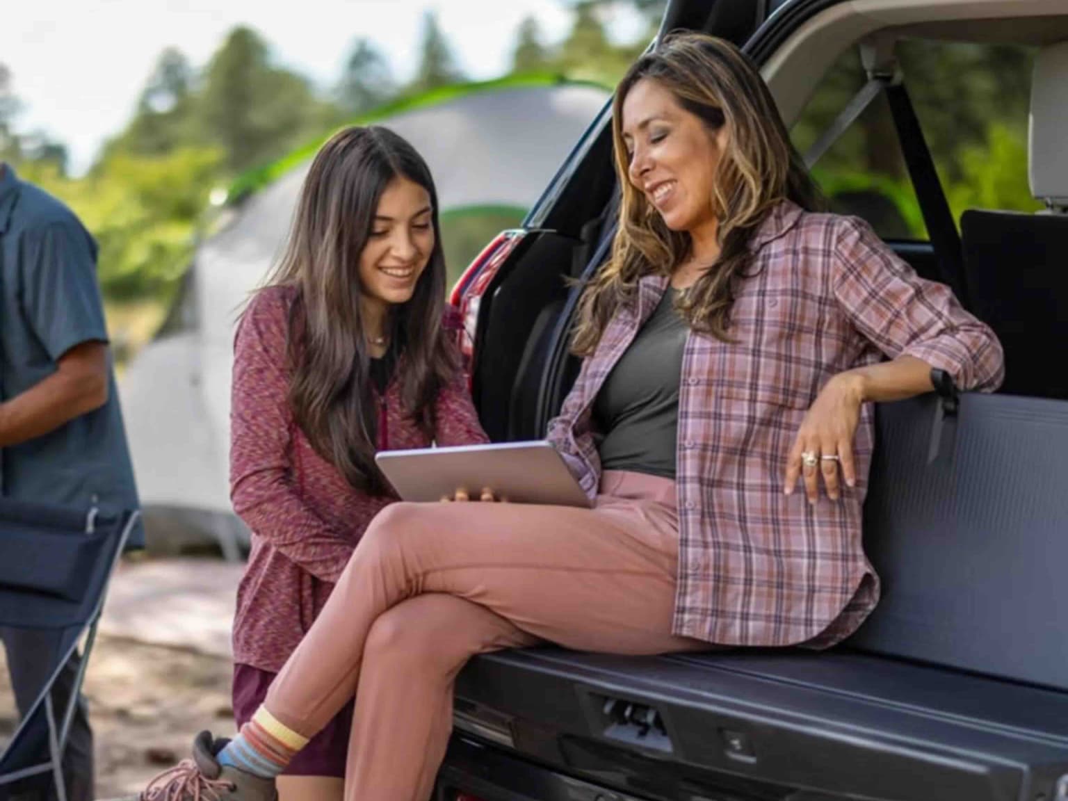 Woman and girl using a tablet in the back seat of a car with outdoor scenery in the background.