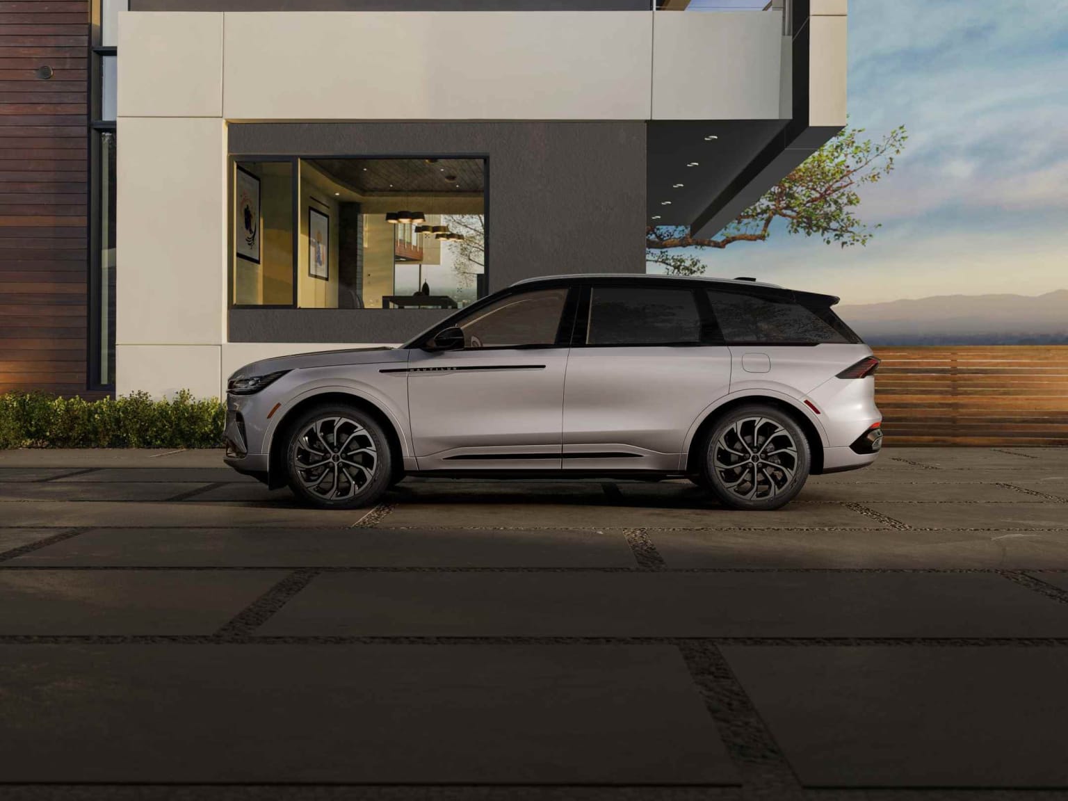 Silver SUV parked in front of a modern building with a glass facade and a small tree in the foreground.