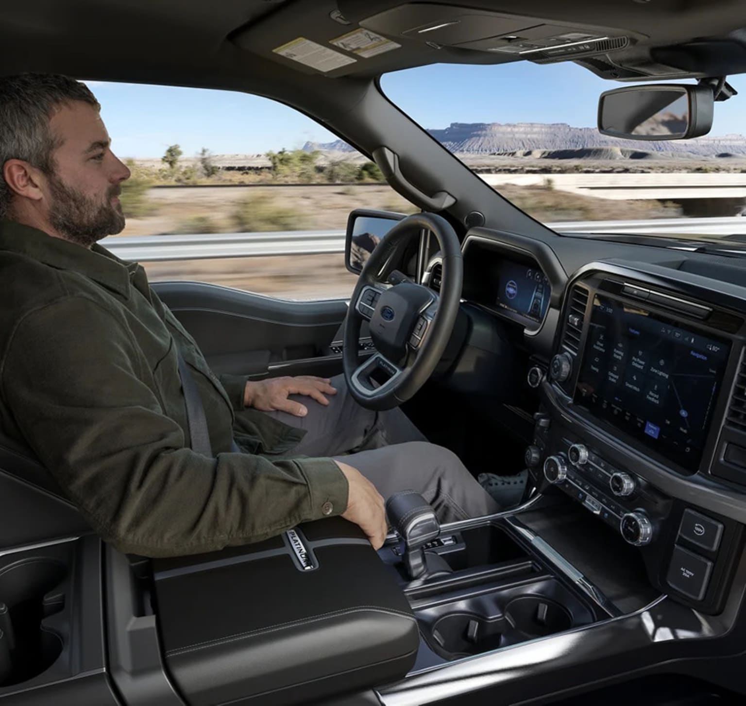 A man driving a car in a desert landscape with mountains in the background.