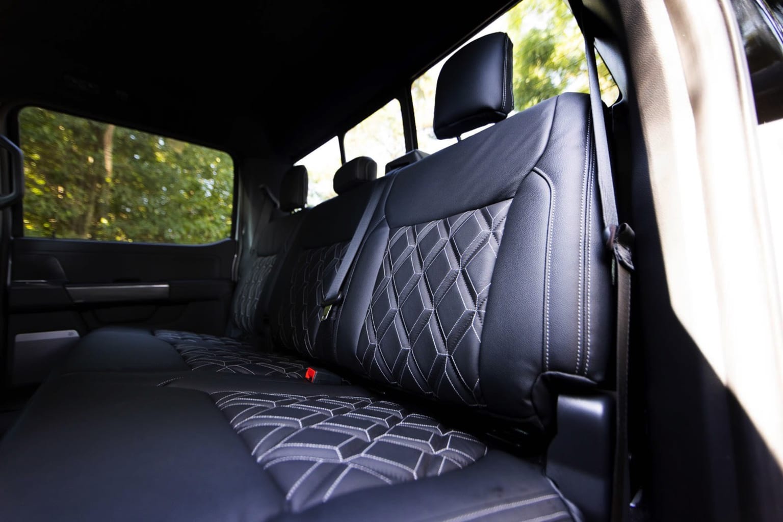 Interior of a vehicle with black leather-upholstered backseat with diamond-patterned design, set against a blurred natural landscape.