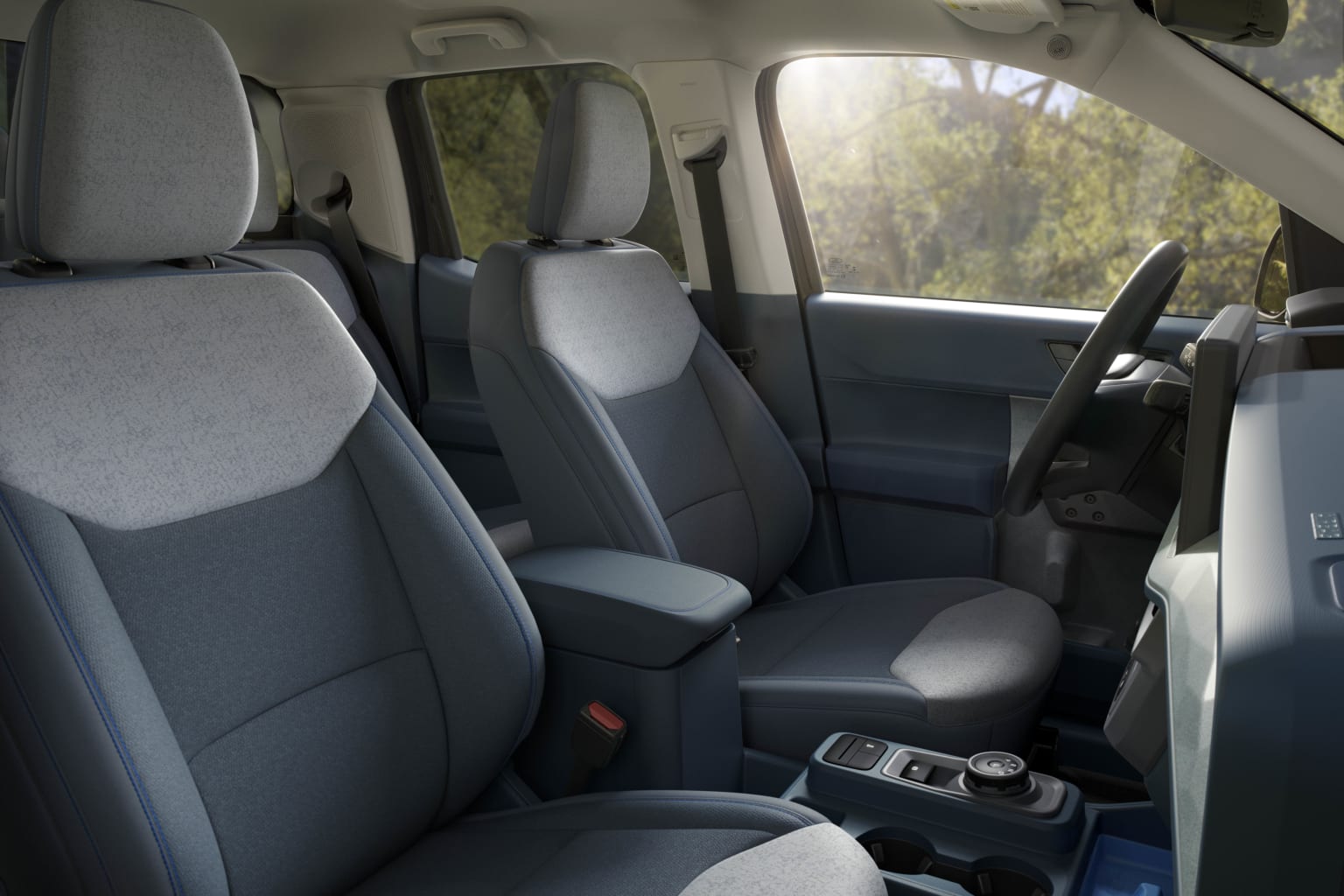 The image shows the interior of a vehicle, with gray upholstered seats and a console in the center. The background outside the vehicle appears to be a natural setting, with trees and greenery visible through the windows.