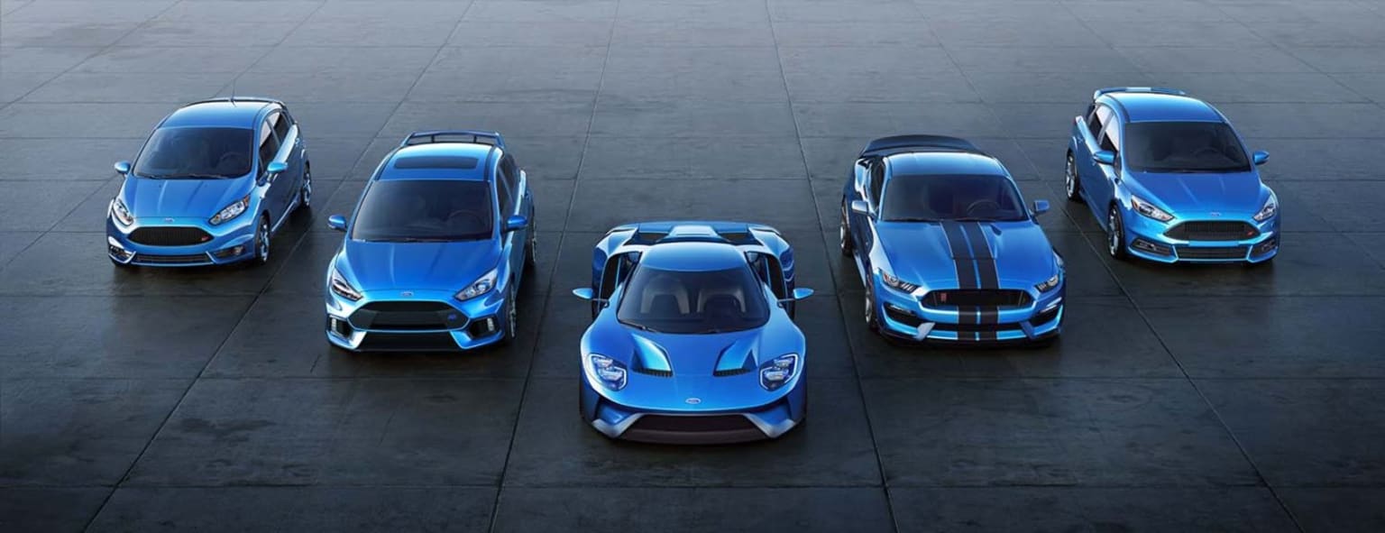 a group of four blue sports cars parked in a parking lot next to each other in front of a building