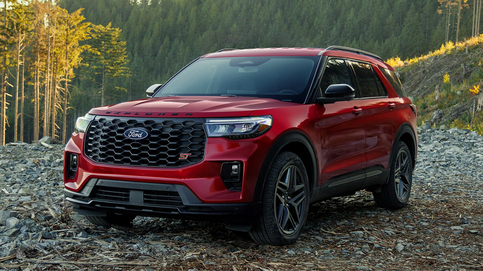 Red SUV parked on rocky terrain with evergreen forest in background.