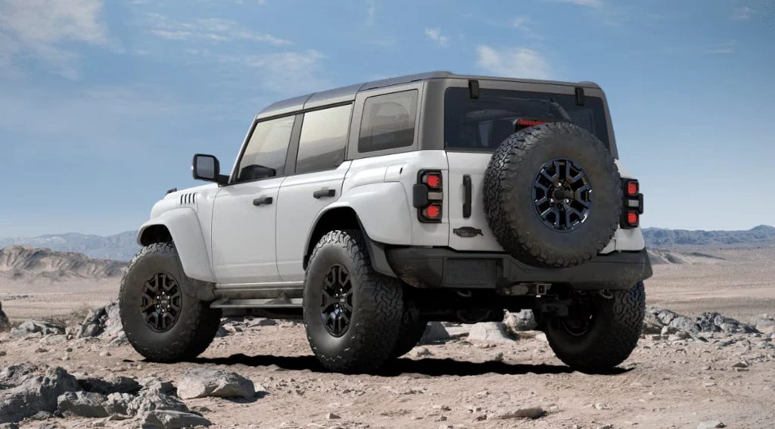 Off-road vehicle on rocky terrain against clear blue sky with clouds.