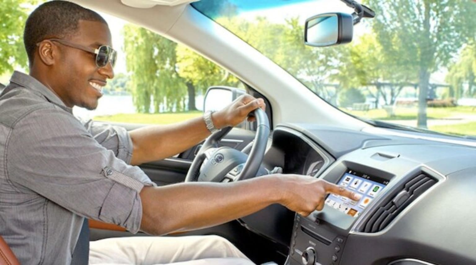 a man sitting in the driver's seat of a car with his hand on the steering wheel and smiling