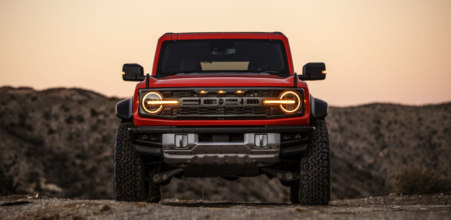 a red truck parked on top of a dirt road next to a mountain covered in grass and bushes at sunset