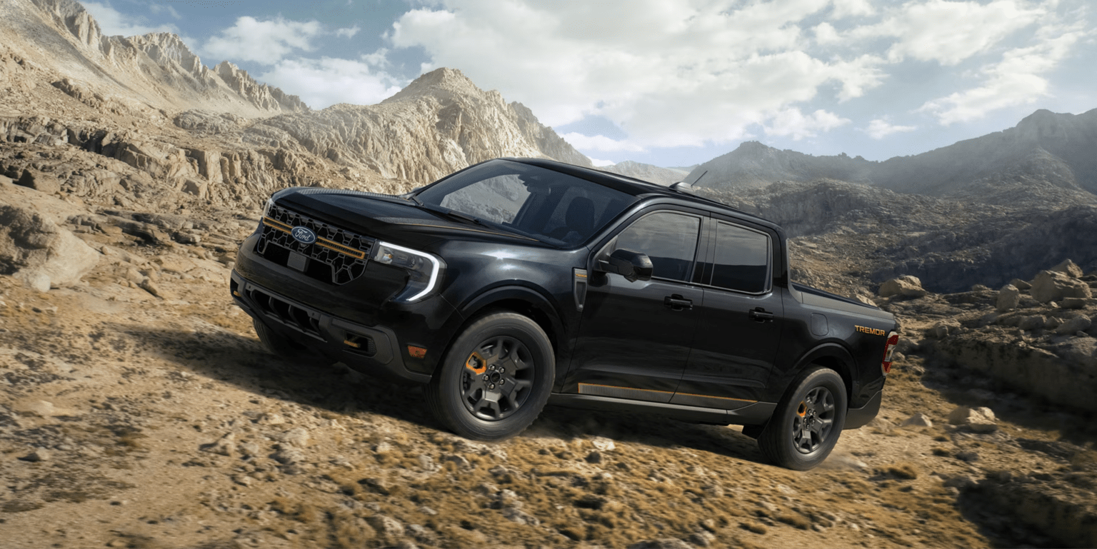 A black pickup truck driving on rocky, mountainous terrain under a cloudy sky.