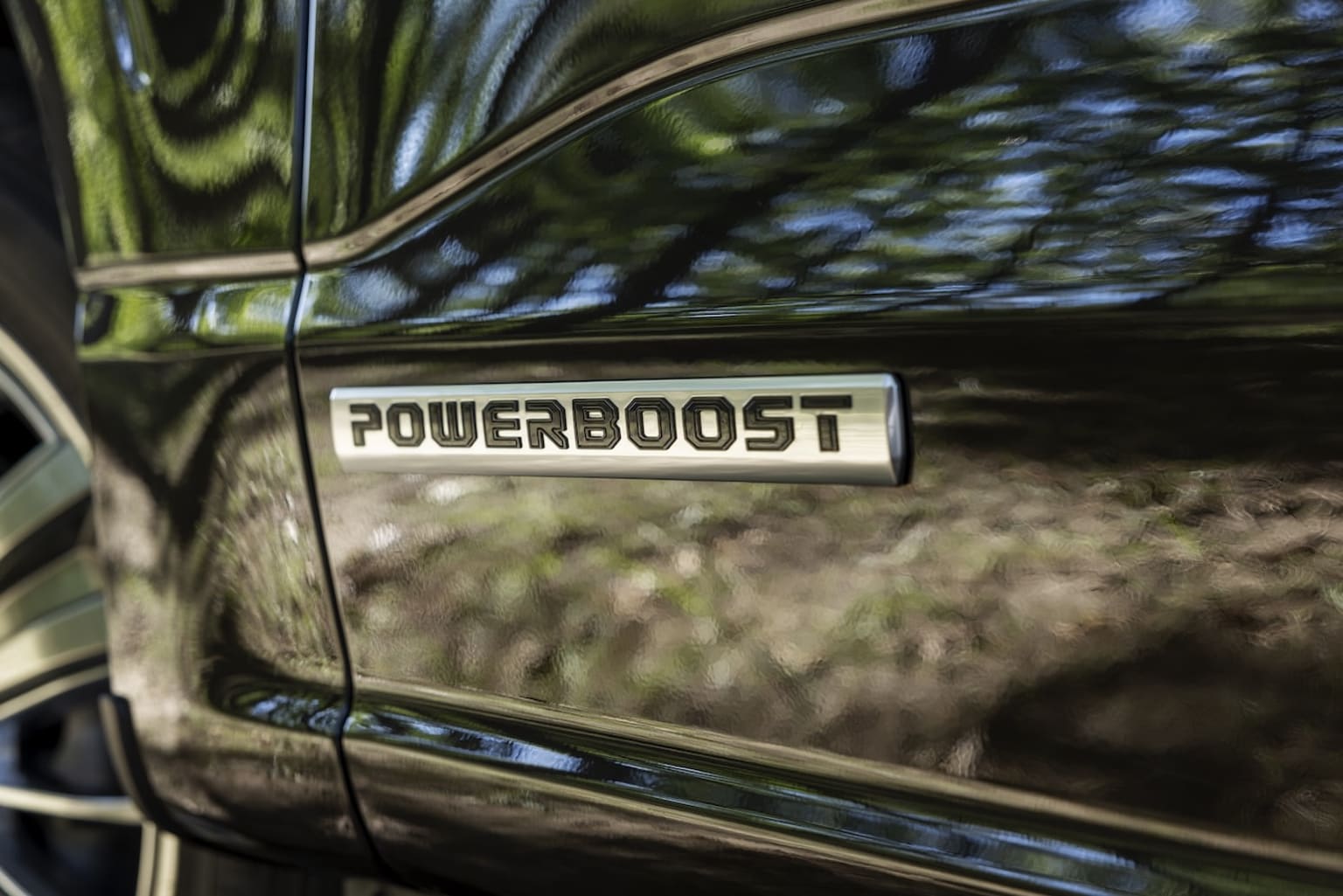 Close-up view of a vehicle's side panel with a "POWERBOOST" label displayed, in a blurred outdoor setting.