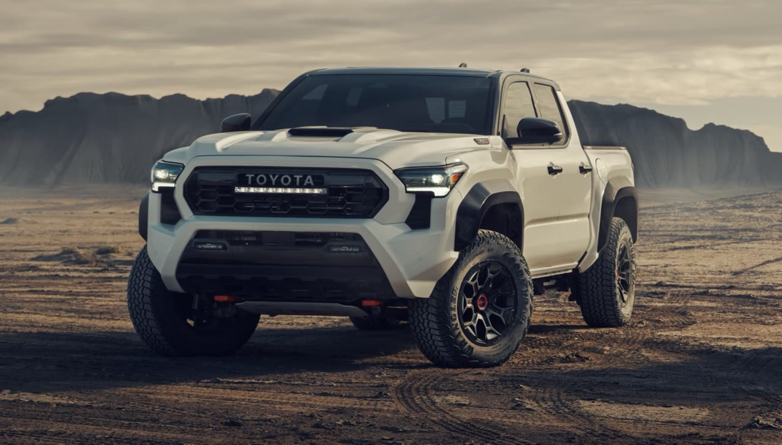 An off-road pickup truck in a desert landscape with mountains in the background.