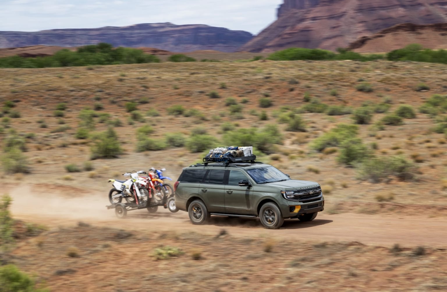 Off-road vehicle driving through desert landscape with horse-drawn carriage and red rock formations.