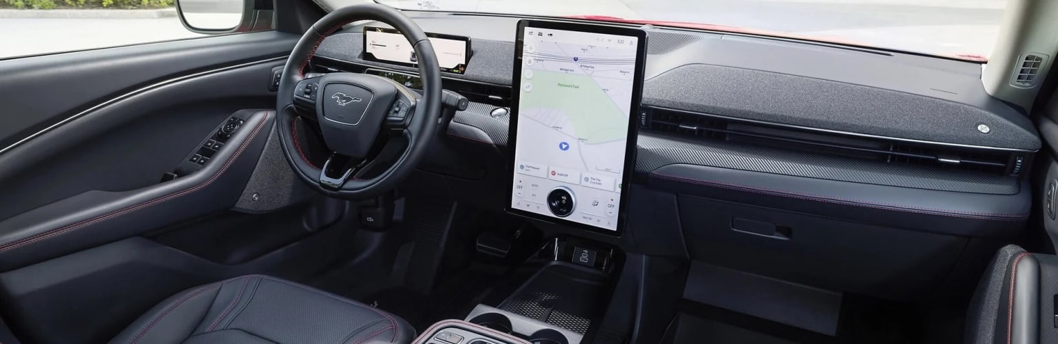 Interior of an electric vehicle with a large touchscreen display on the dashboard and a steering wheel with various controls. The background shows a sleek and minimalist design.