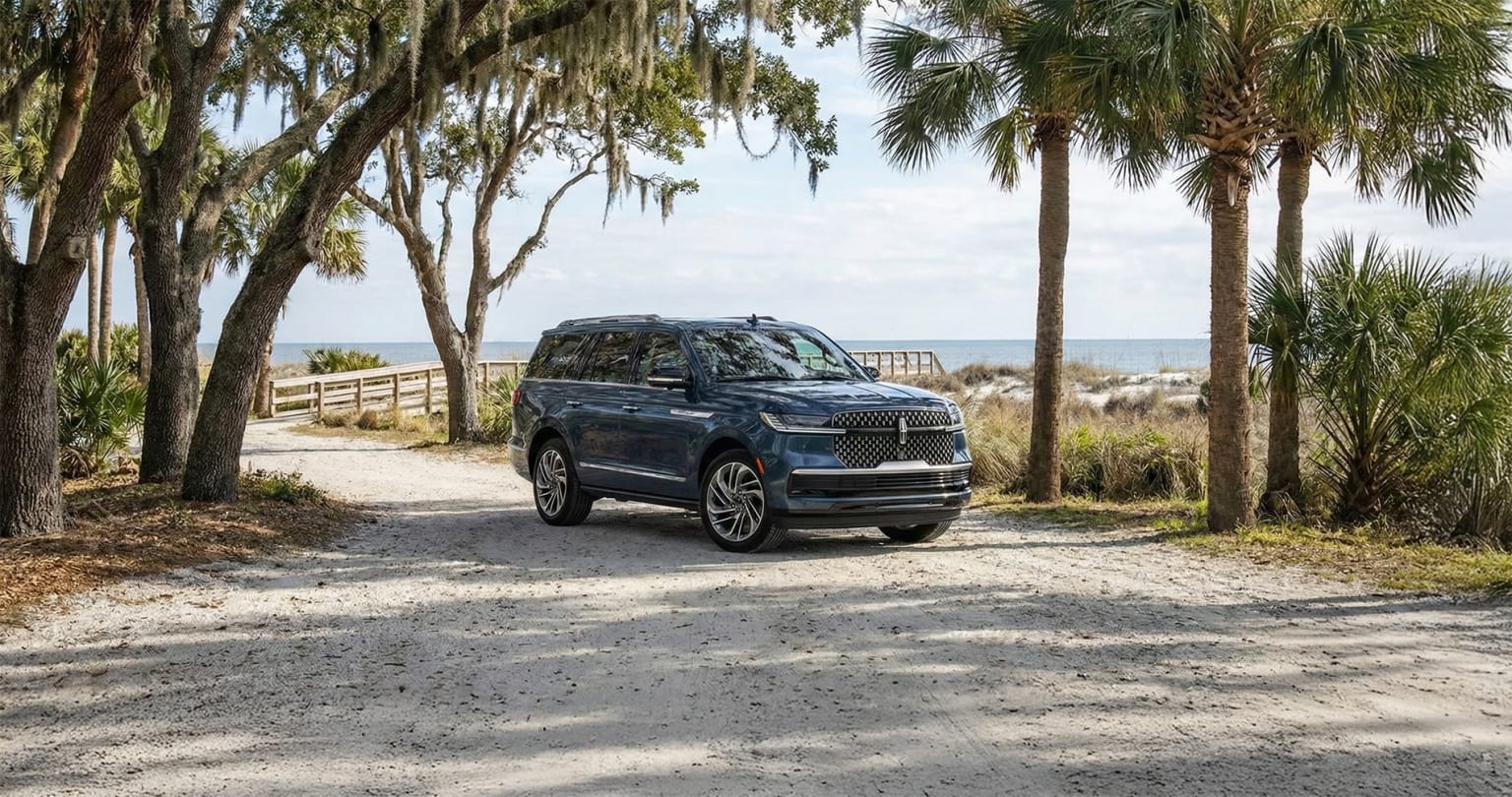 SUV parked on a dirt path with palm trees and ocean in the background.