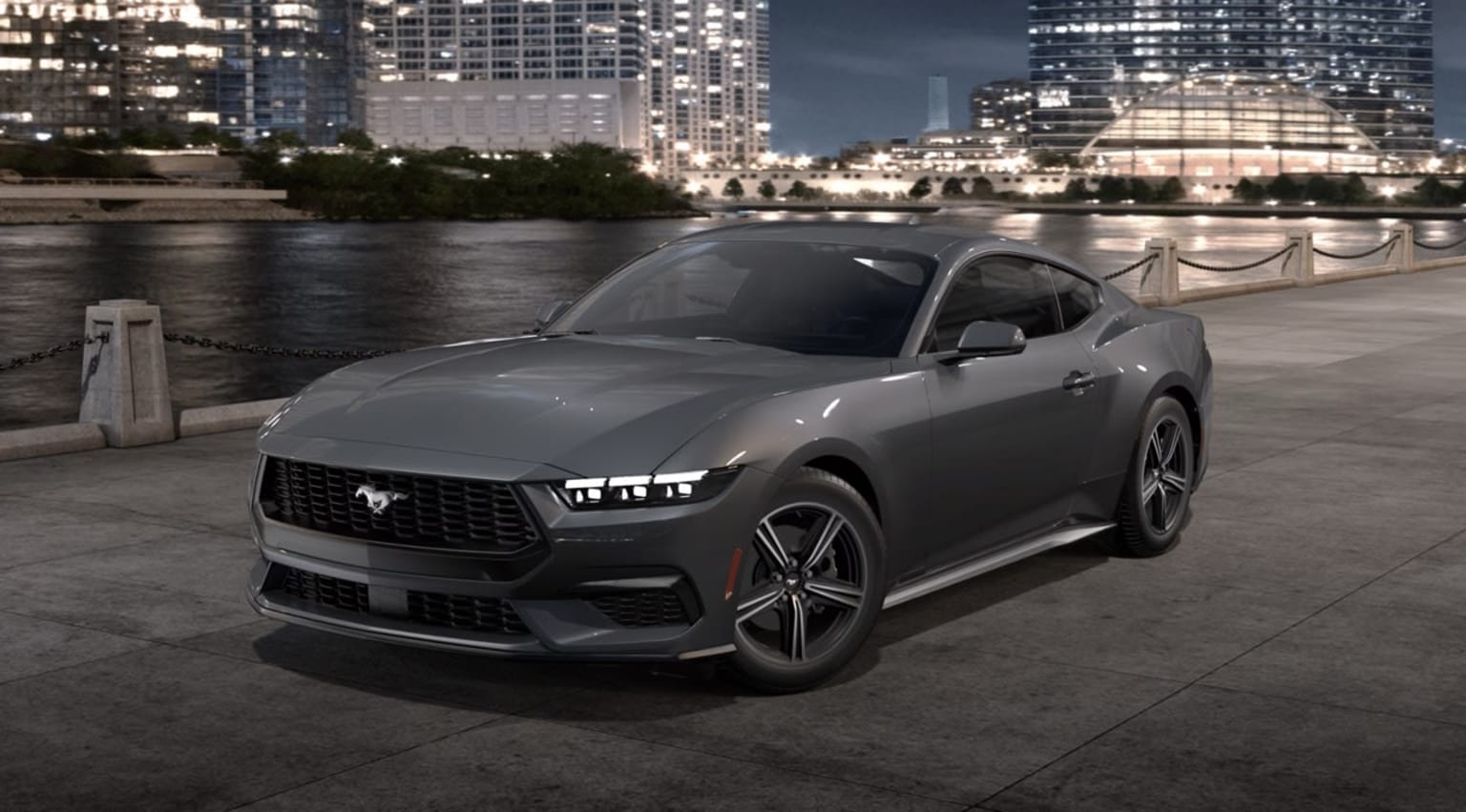 A sleek, gray sports car parked on a waterfront promenade, with a backdrop of illuminated high-rise buildings and a nighttime cityscape.