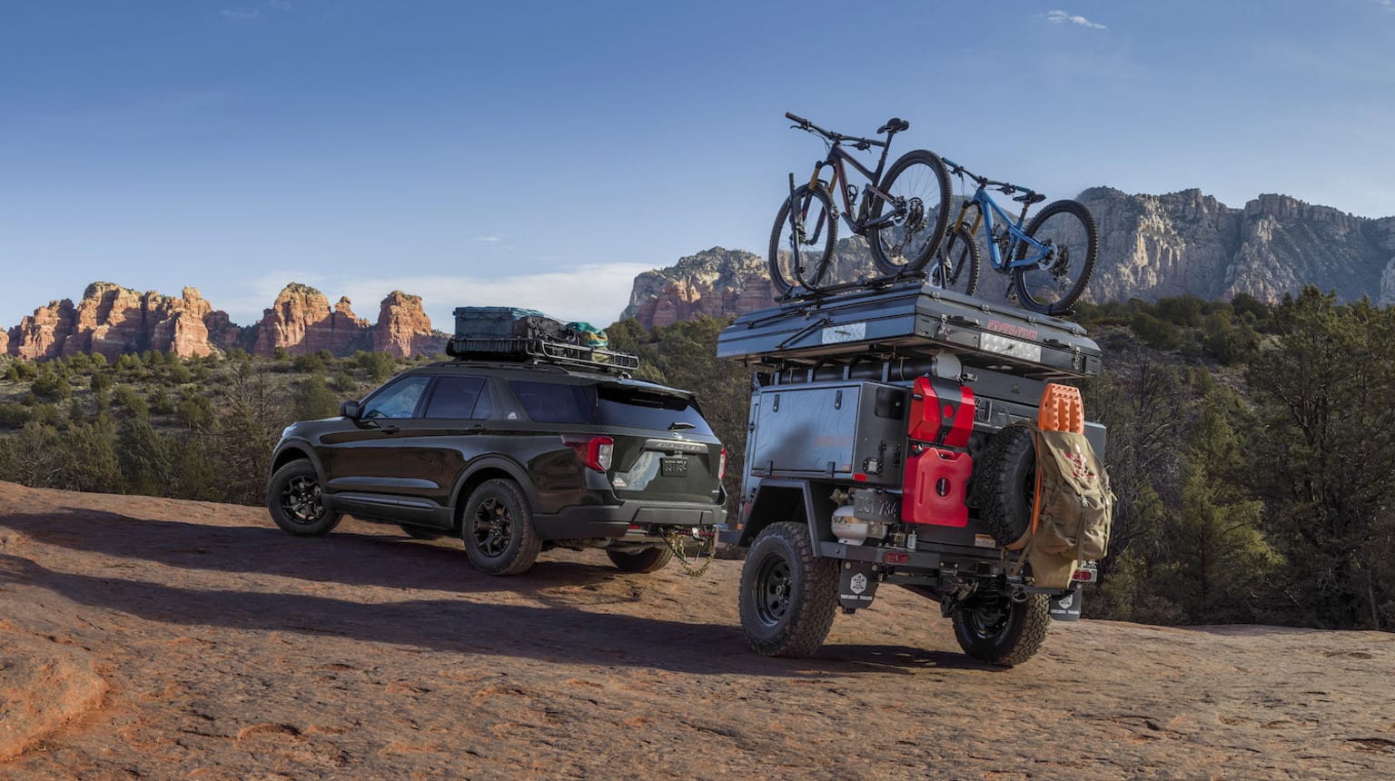 a jeep with a bike on top of it parked on a dirt road next to a truck with a bike on top of it