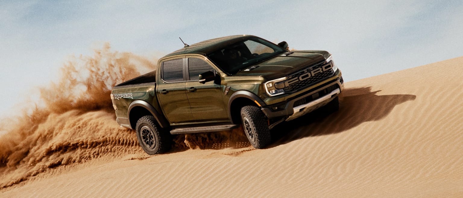 Off-road pickup truck driving through a desert landscape kicking up sand.