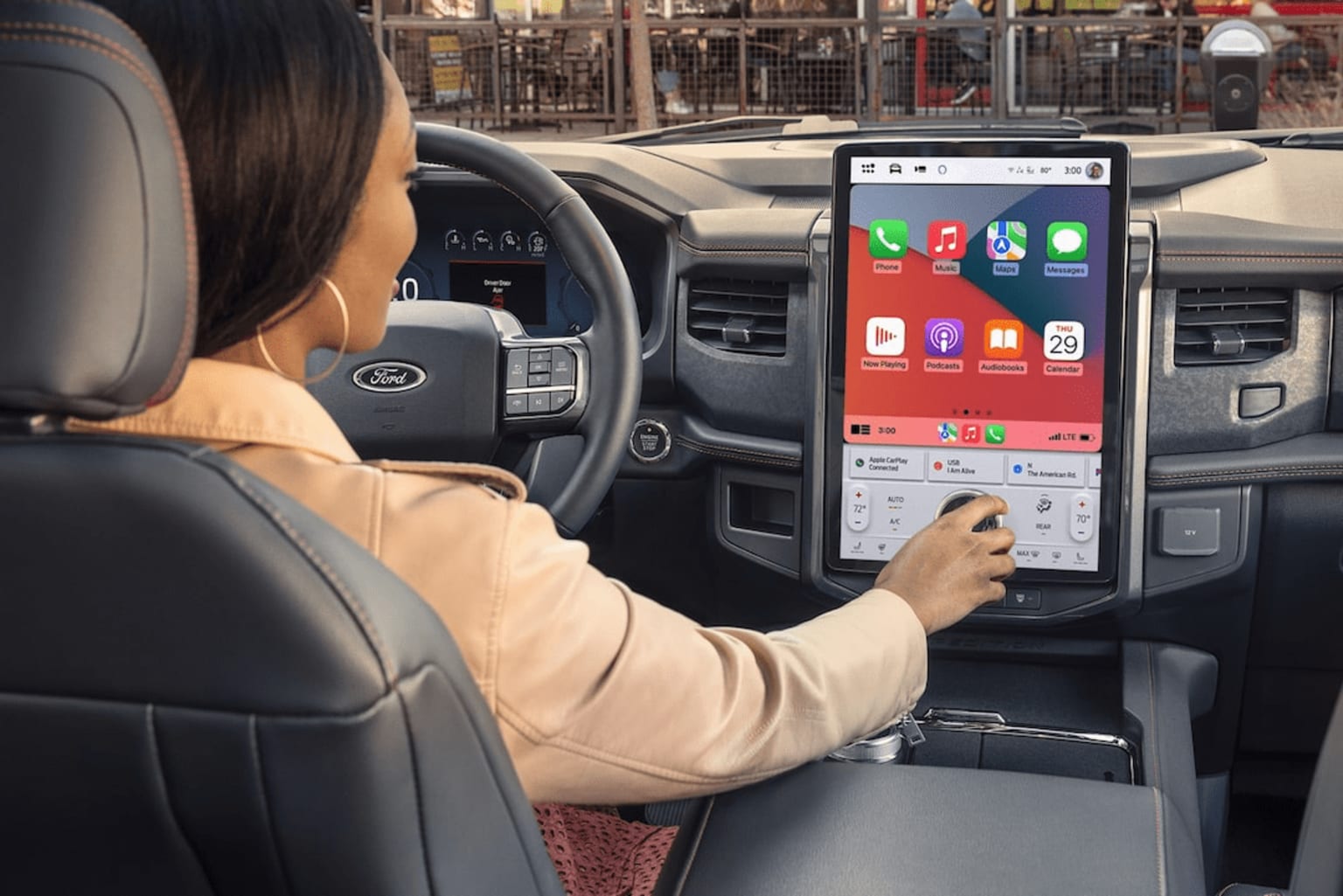 The image depicts the interior of a vehicle with a person sitting in the driver's seat and interacting with a touchscreen display on the dashboard.