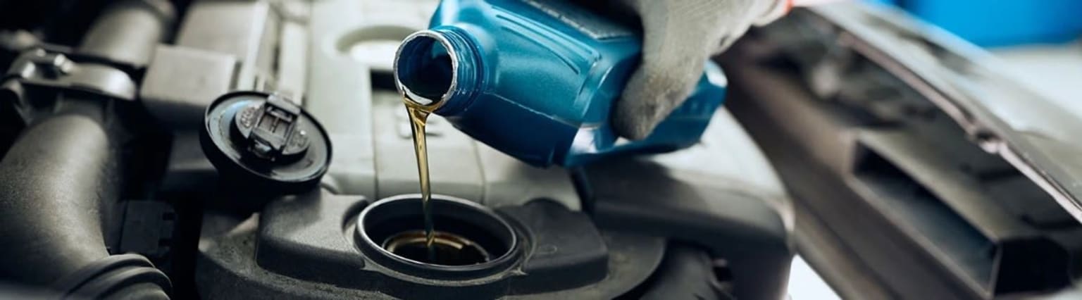 Blue oil container pouring oil into a dark receptacle in an automotive or industrial setting.