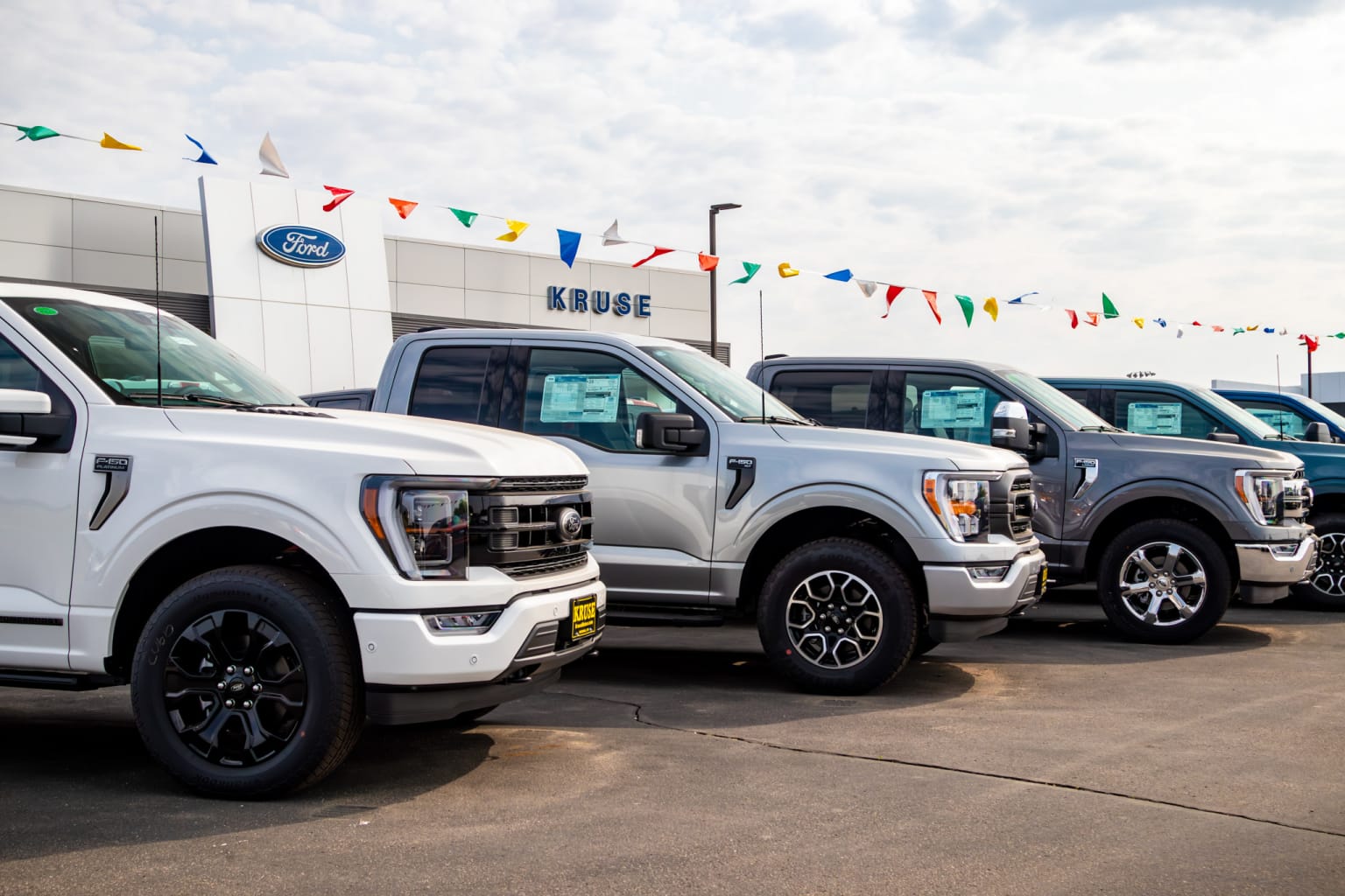 a row of white ford trucks parked in front of a ford dealership with flags in the back ground