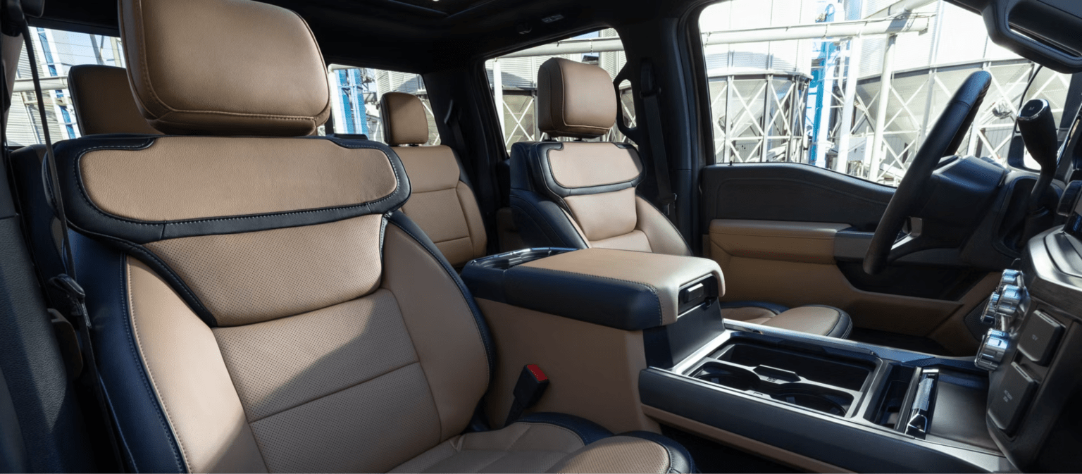 Tan and black leather seats fill the foreground of a vehicle interior, with an industrial facility visible through the windows in the background.