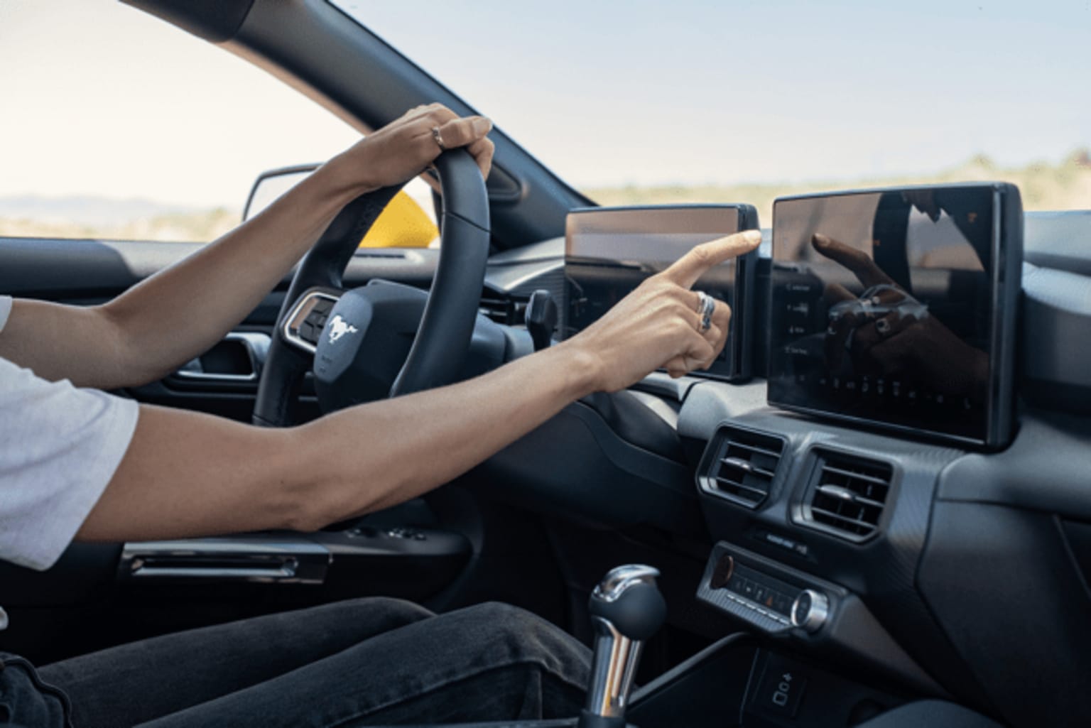 Interior of a car with the driver's hands on the steering wheel and a tablet or smartphone mounted on the dashboard.