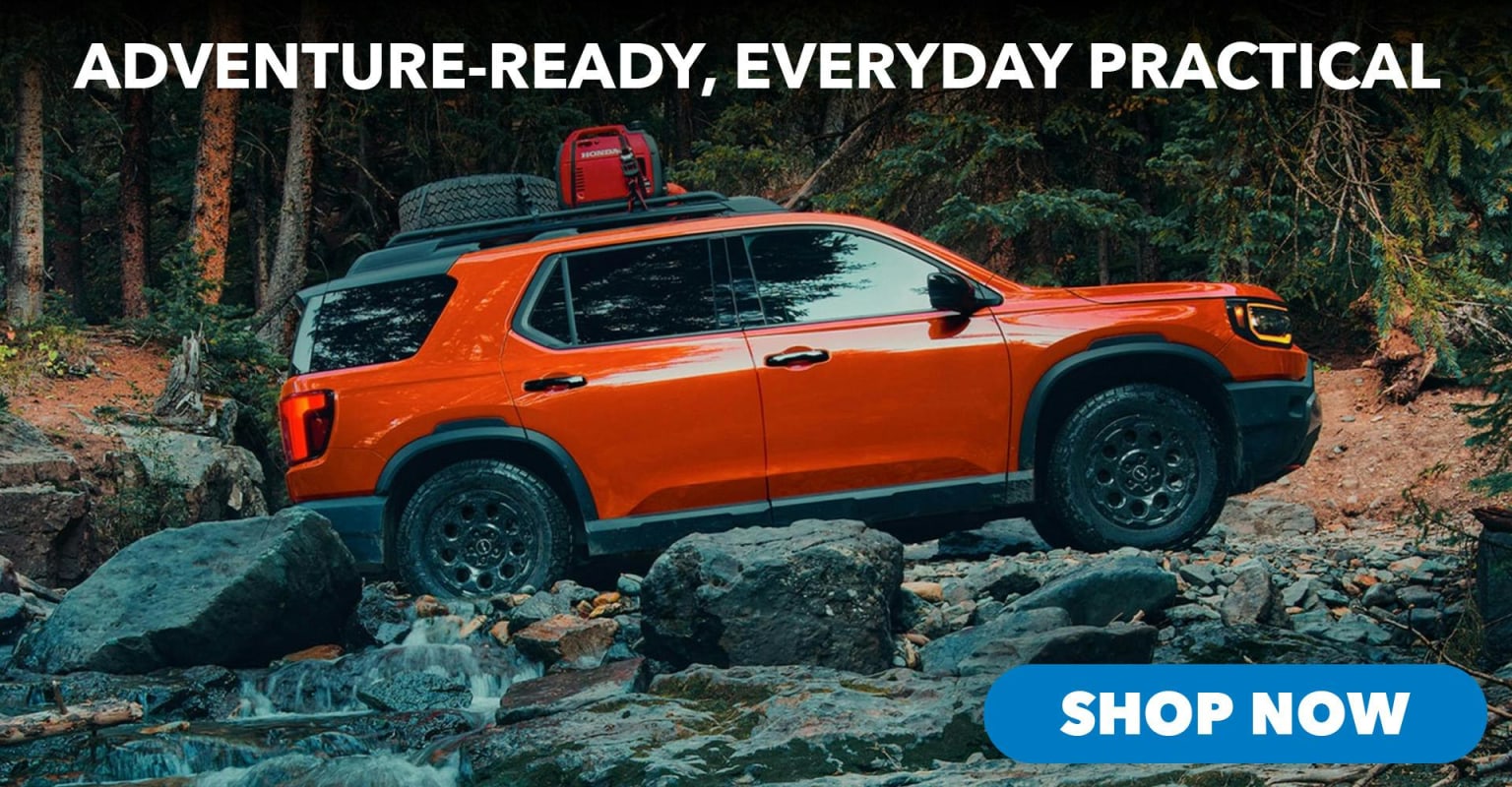 An orange SUV with gear on its roof navigating a rocky stream bed in a forest.