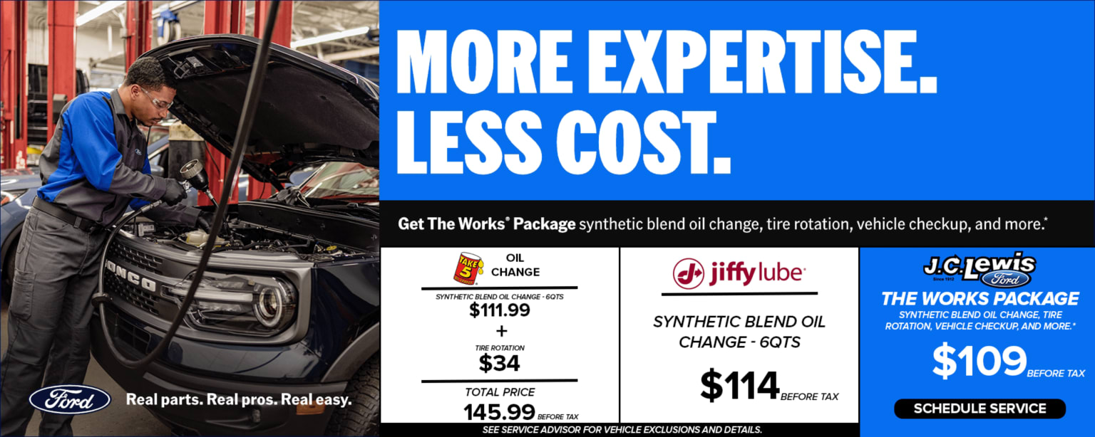 A mechanic working on a car in a garage with an advertisement for car service packages in the background.