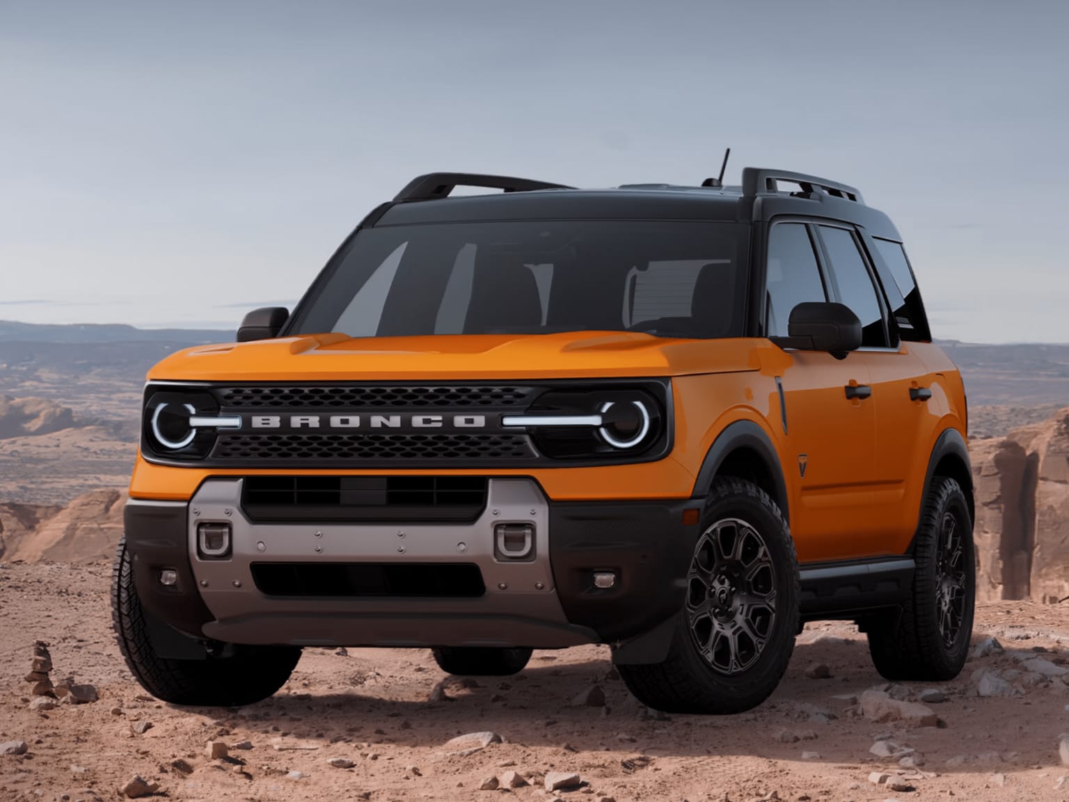 An orange off-road SUV parked on rocky desert terrain with distant red rock formations and a clear sky.